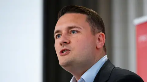 Reuters Wes Streeting speaking at a conference and appears to be mid sentence. He is wearing a light blue shirt and a dark blazer jacket 