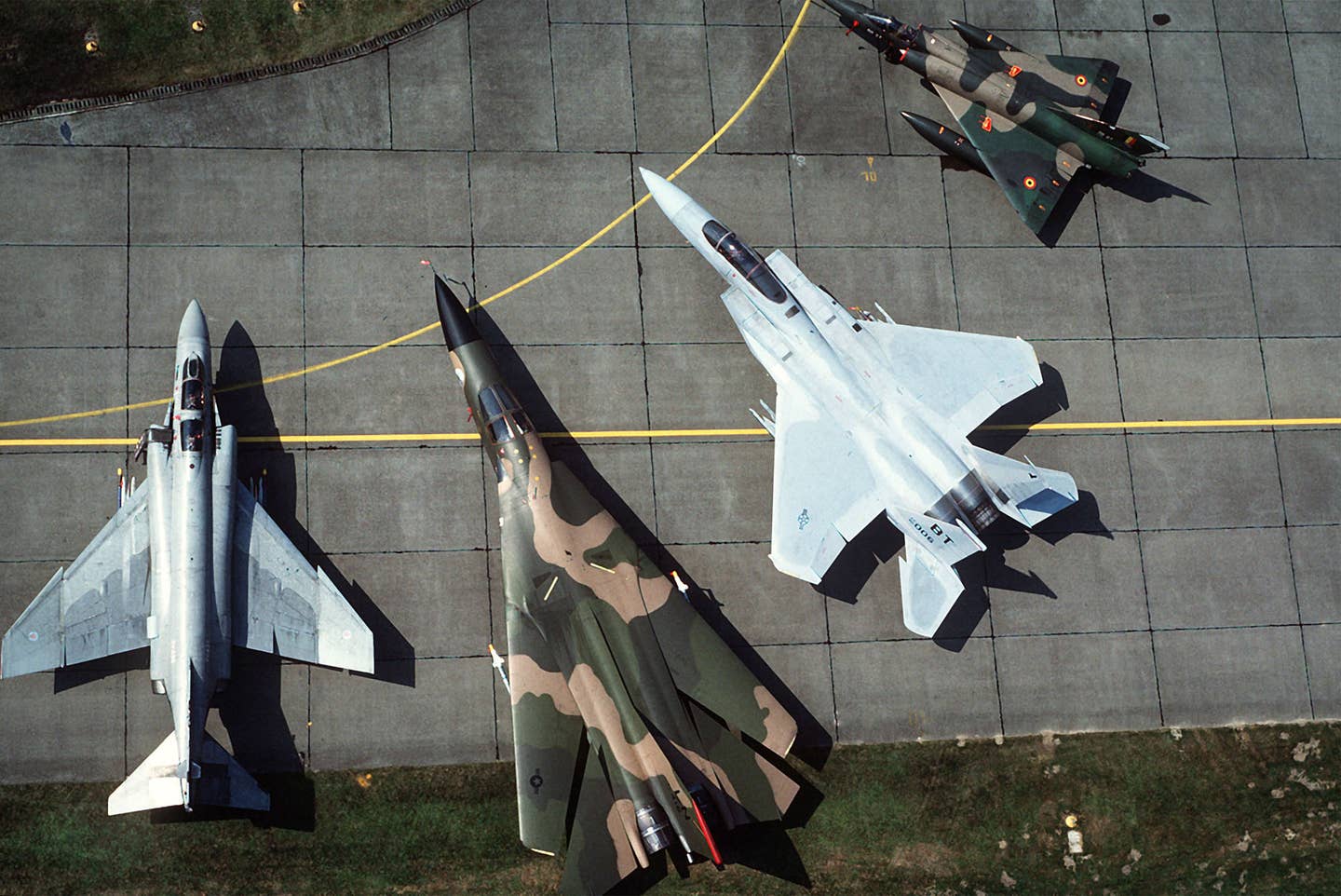 An aerial view of a portion of the NATO airpower on the Central Front in the 1980s. From left: a U.K. Royal Air Force Phantom FGR2, a USAFE F-111, a USAFE F-15C from Bitburg Air Base in Germany, and a Belgian Mirage 5. <em>U.S. Air For</em>ce