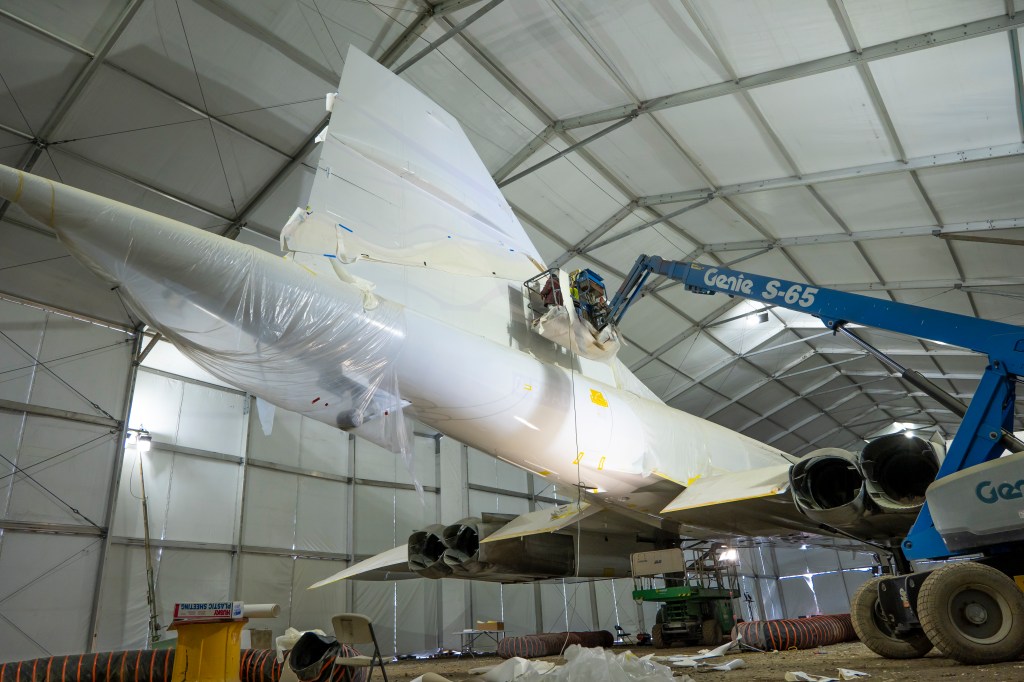 workers in a small cherry picker paint the tail fin of the Concorde inside a large tent at The Brooklyn Navy Yard, Brooklyn, New York
